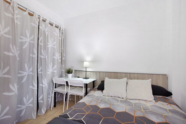 A hotel room with a bed, a desk, a chair, and a lamp.
