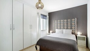 A bedroom with a bed, bedside tables, a wardrobe, and a patterned headboard.