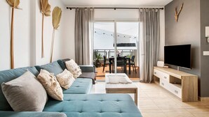 Una sala moderna con sofá, televisión y balcón con mobiliario exterior.