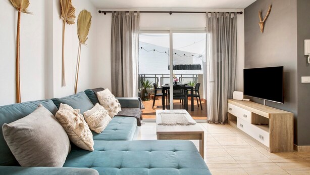 A modern living room with a sofa, TV, and a balcony with outdoor furniture.