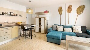 A modern living room with a blue sofa, a wooden coffee table, and a kitchen area with a dining table and chairs.