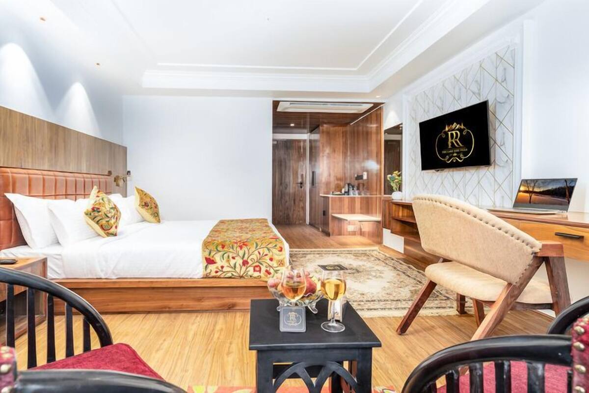 A hotel room with a bed, a desk, a chair, a TV, and a small table with glasses.