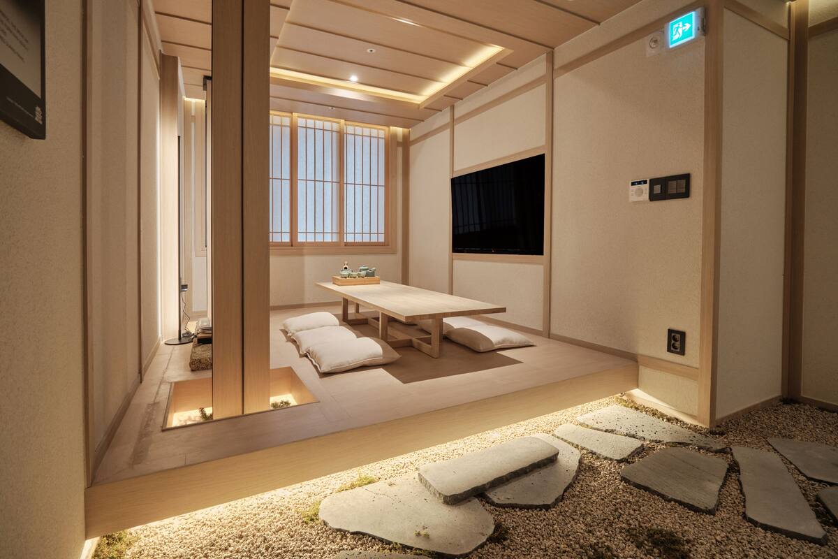 Una habitación de estilo japonés tradicional, con suelo de tatami, una mesa baja con cojines y una puerta corredera que da a otra estancia.