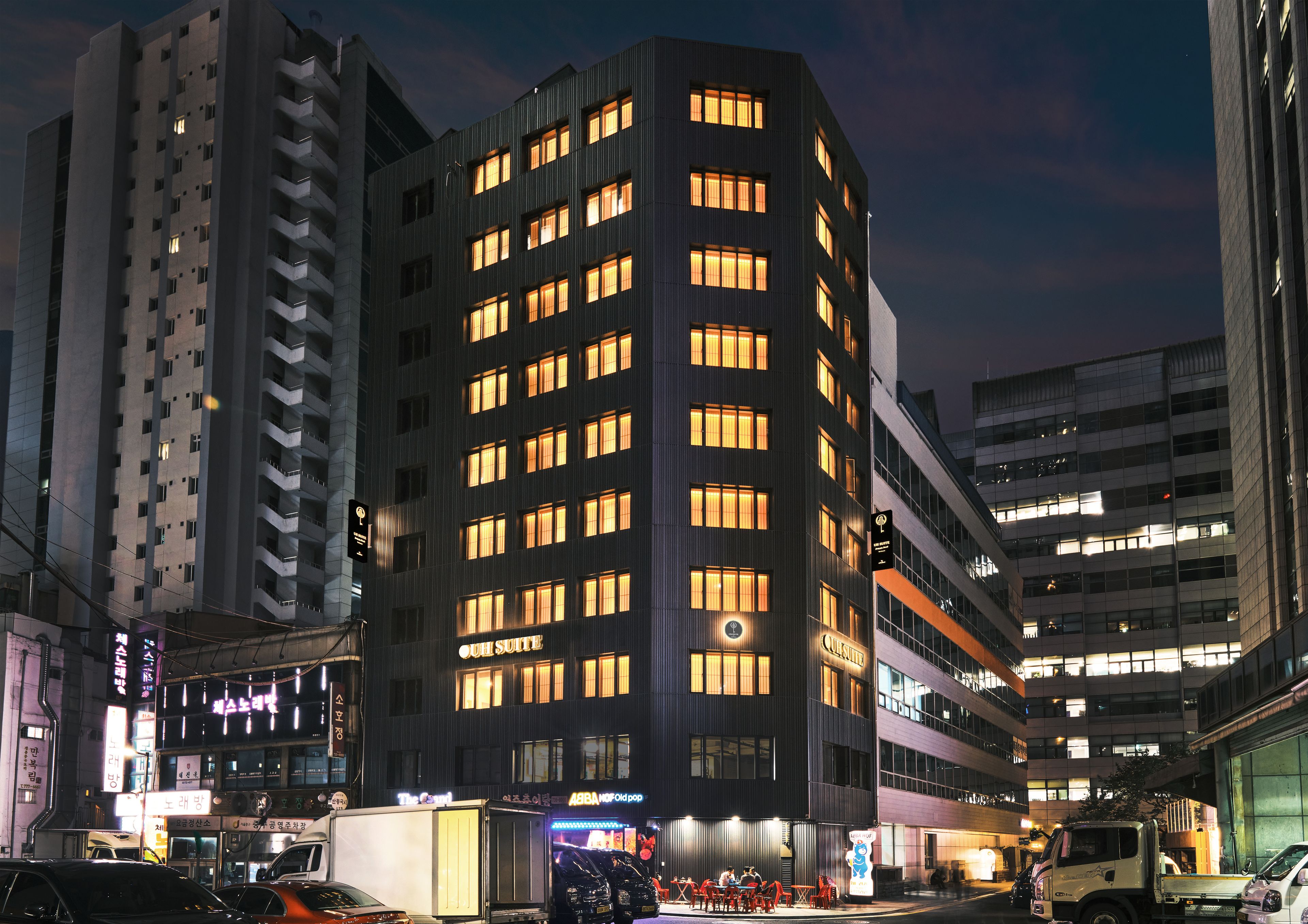Un hôtel à plusieurs étages au design moderne, avec une enseigne bien visible indiquant « The Suite », de nombreux balcons et une façade bien éclairée.