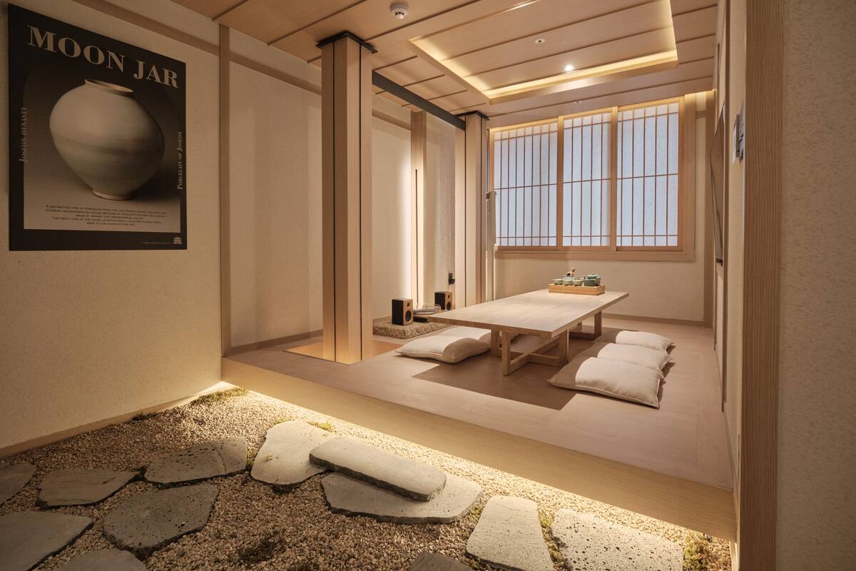 Una habitación tradicional japonesa con suelo de tatami, una mesa baja, cojines y un ventanal con puertas shoji.