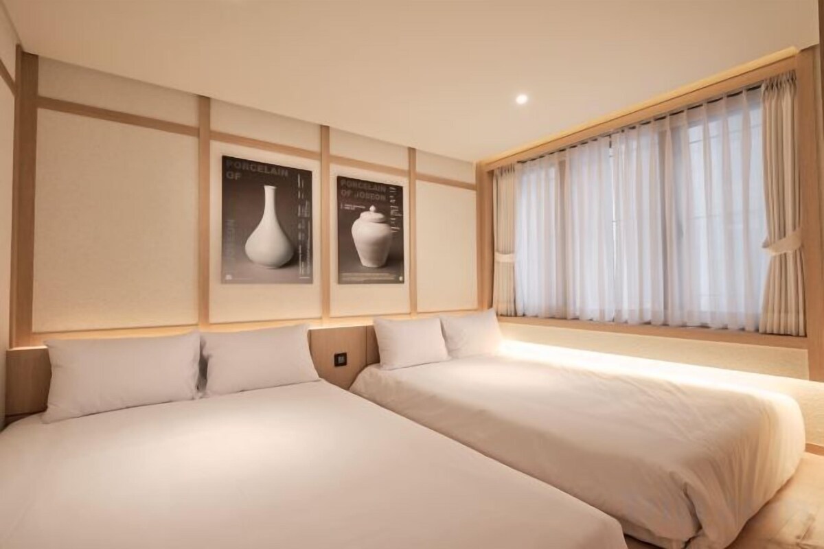 A hotel room with two beds, a large window with curtains, and wall-mounted artwork.