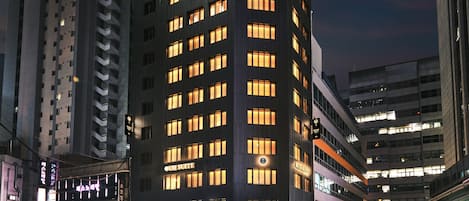A multi-story hotel with a modern design, featuring a prominent 'The Suite' sign, multiple balconies, and a well-lit facade.