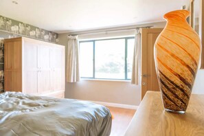 A bedroom with a bed, a wooden nightstand, a large vase, and a window with curtains. - Lush & Spacious 3BD House - East Brighton (Brighton)