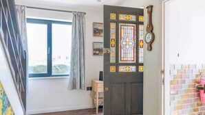 Una stanza con pavimento in legno, una porta con vetrata colorata, un orologio e una finestra con tende.