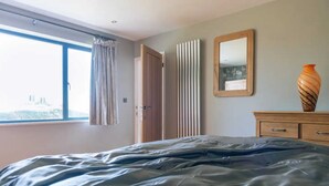 Una camera da letto con un letto grande, una finestra con tende, un termosifone, un comò in legno e uno specchio a parete.