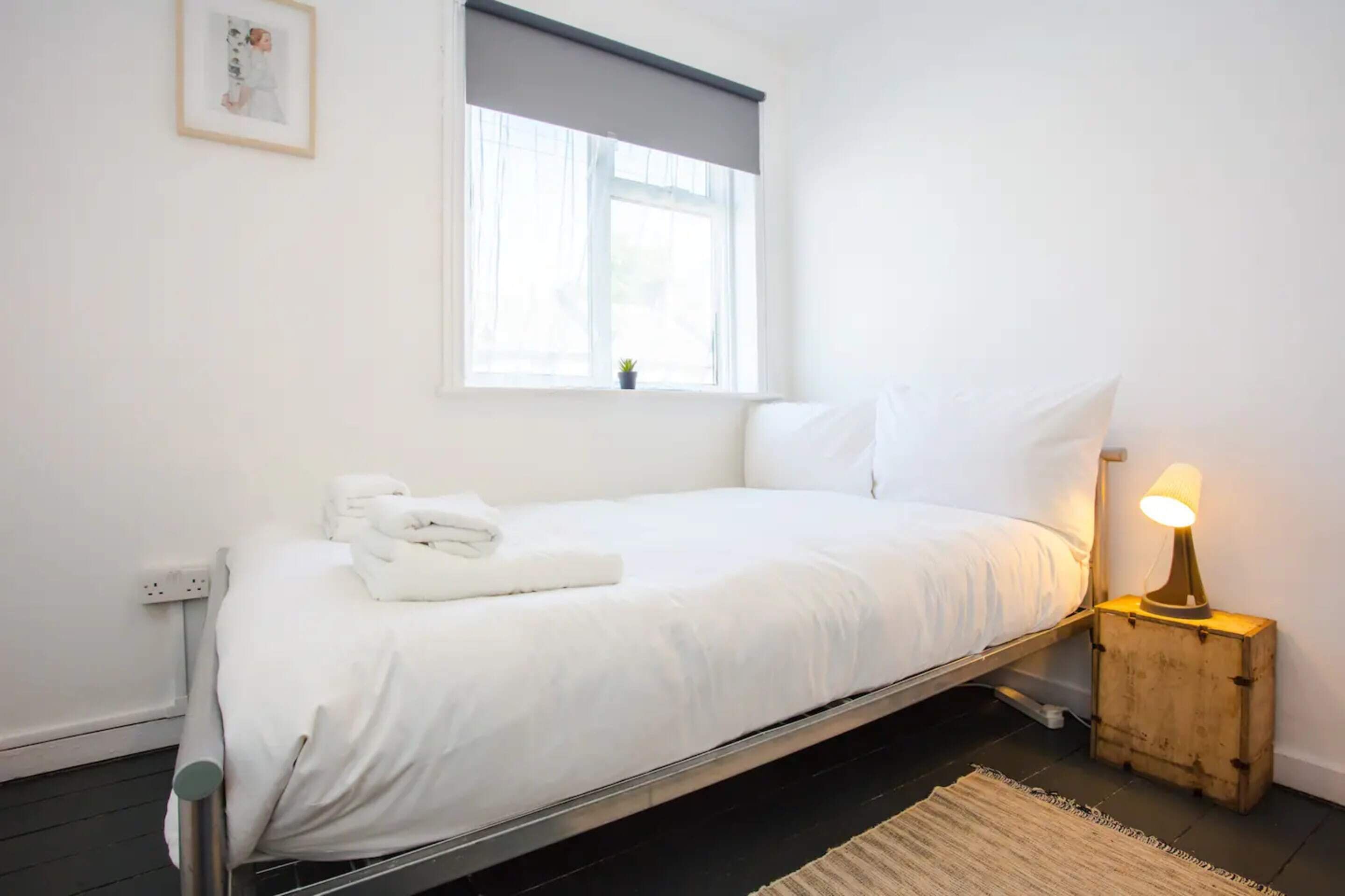 A neatly made bed with white linens, a bedside lamp, and a small potted plant on the windowsill.