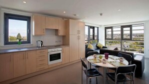 Una cocina moderna con armarios de madera, una zona de comedor con mesa y sillas, y ventanas amplias que ofrecen vista a la ciudad.