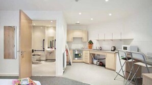 Una cocina compacta equipada con microondas, hervidor y un pequeño comedor con una silla.