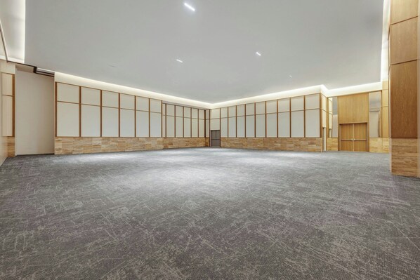 Una habitación amplia con piso alfombrado, paneles de madera y luces empotradas en el techo.