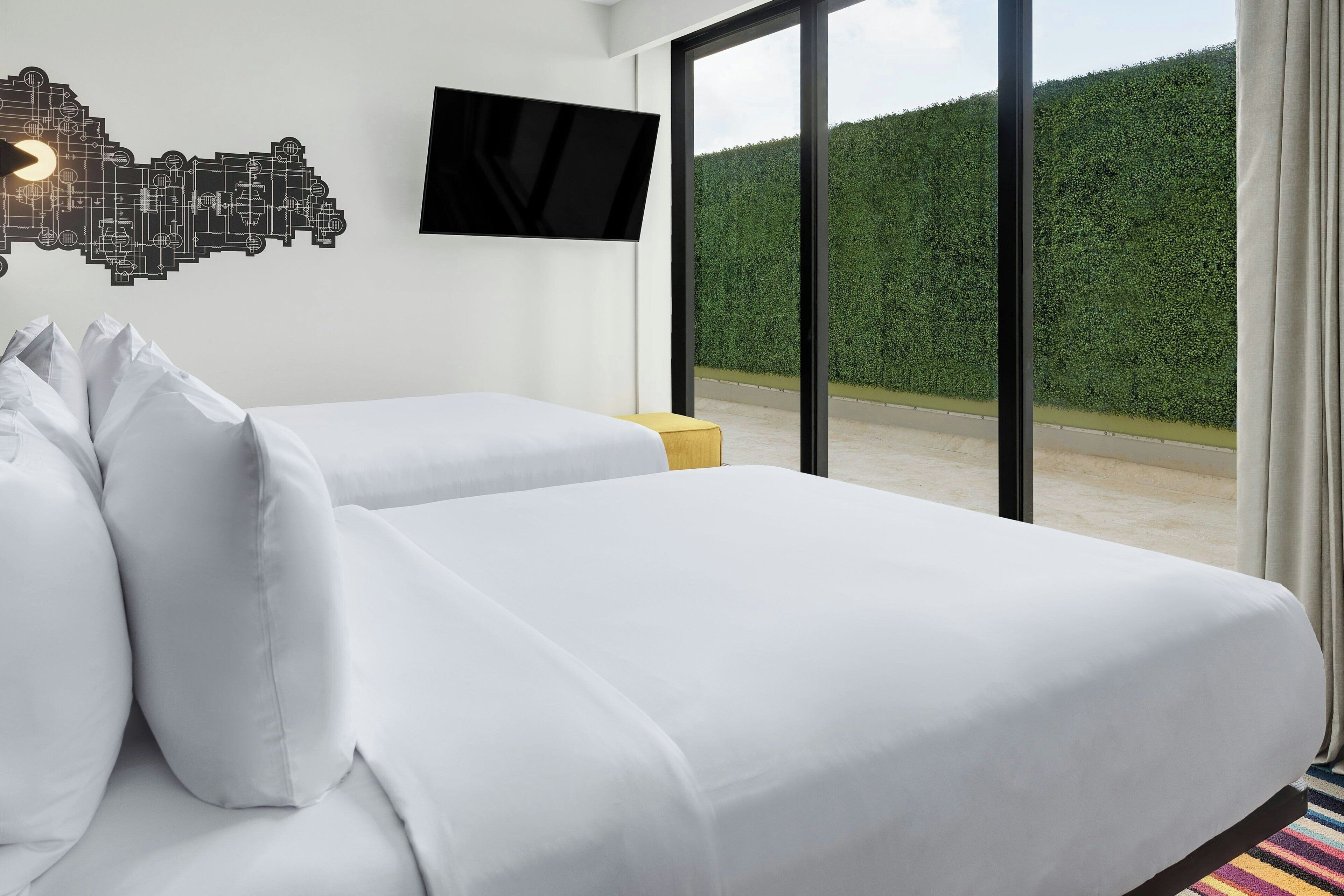 Une chambre d’hôtel avec deux lits, un téléviseur à écran plat et une grande fenêtre donnant sur un bosquet.