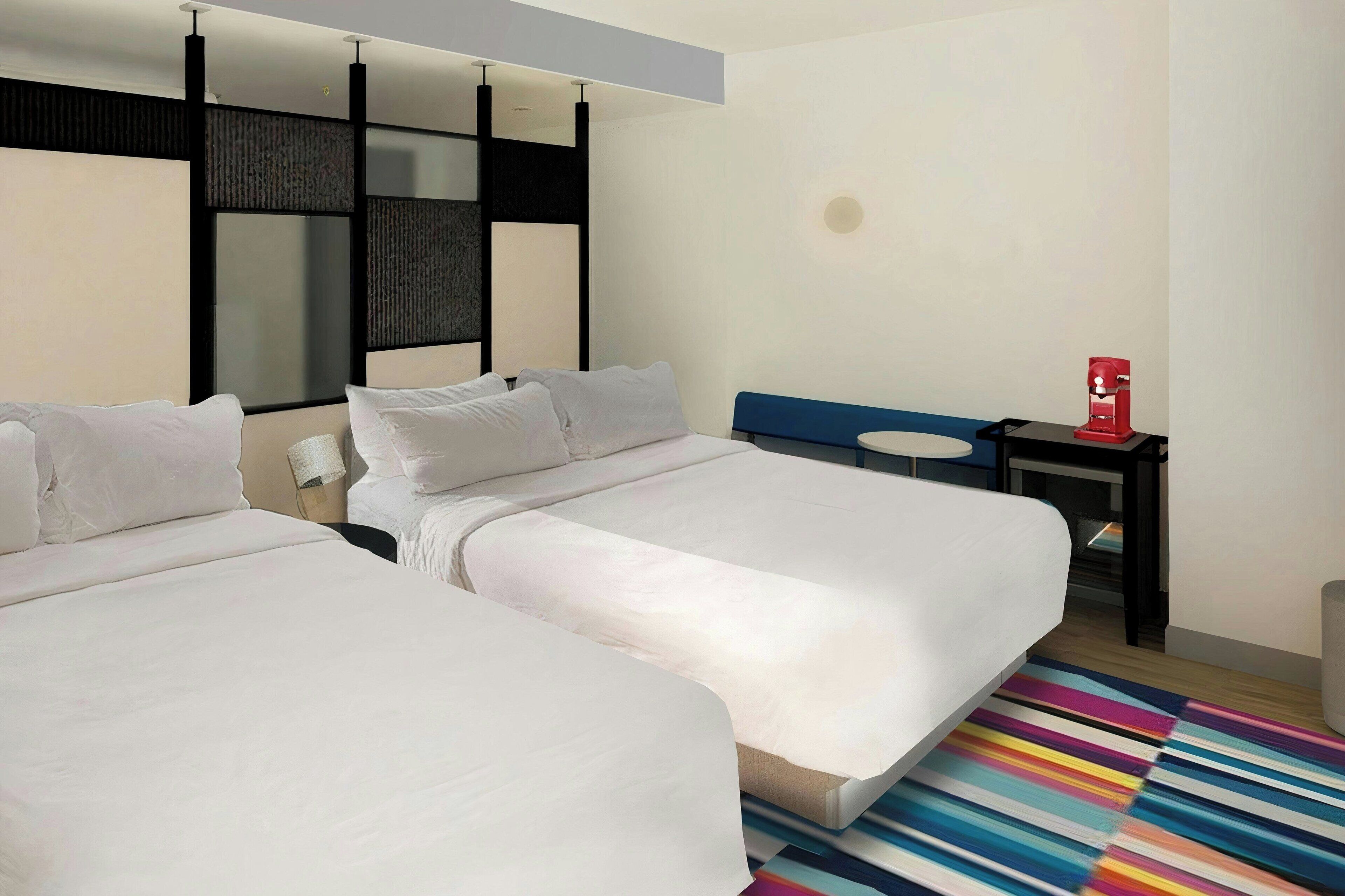 A hotel room with two beds, a desk, a red coffee machine, and a colorful striped rug.