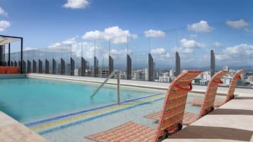 Una piscina en la azotea con agua cristalina, barandilla de vidrio y vista panorámica de la ciudad.