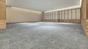 A spacious room with a grey carpet, wooden panel walls, and recessed ceiling lighting.