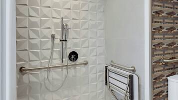 A bathroom with a geometric tile pattern, a shower with a handheld showerhead, and a towel rack.