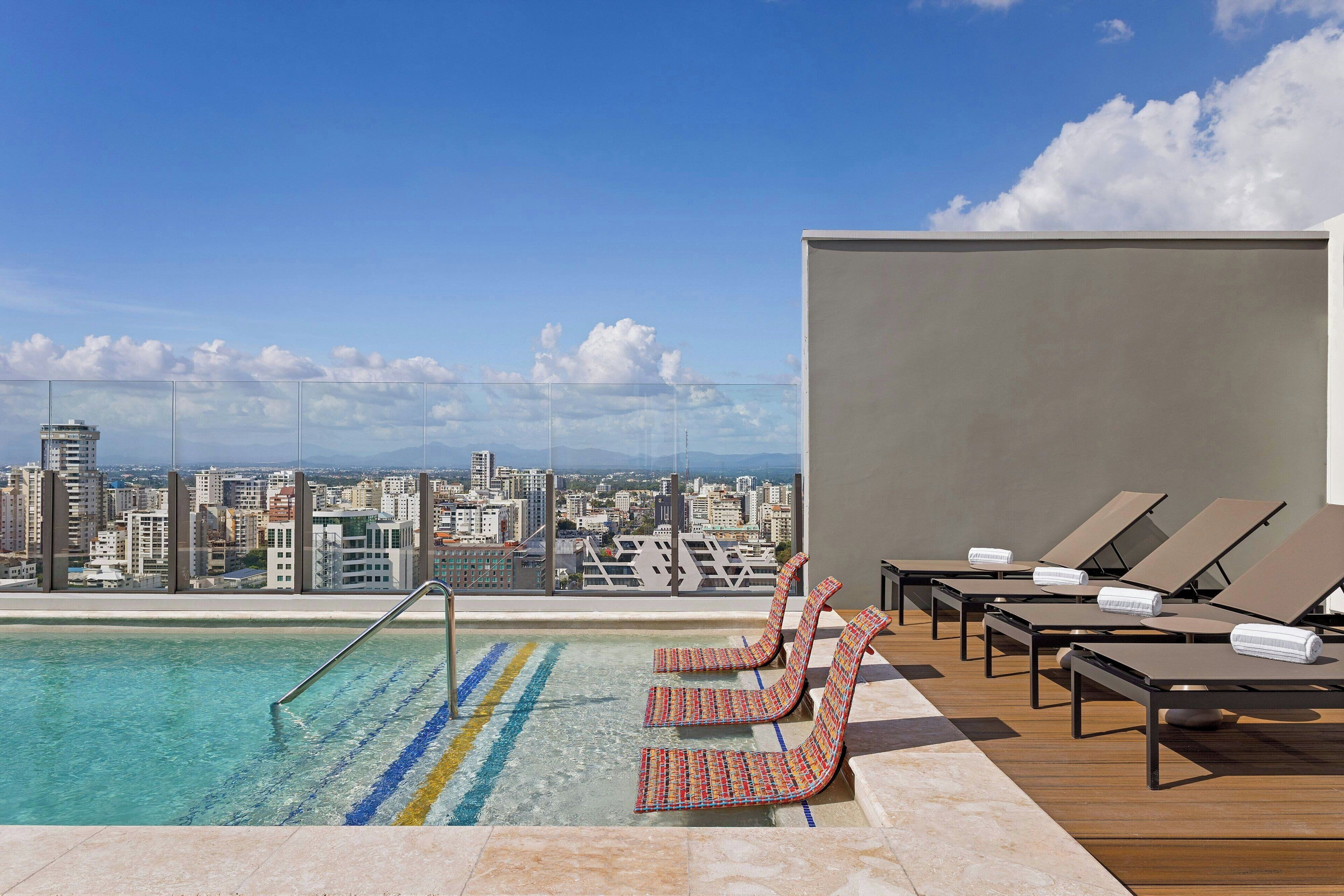Piscina no terraço com espreguiçadeiras e vista para a cidade.