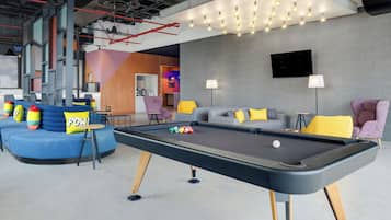 Una mesa de billar con bolas, un sofá con cojines coloridos, e interiores modernos con tuberías y luces a la vista.