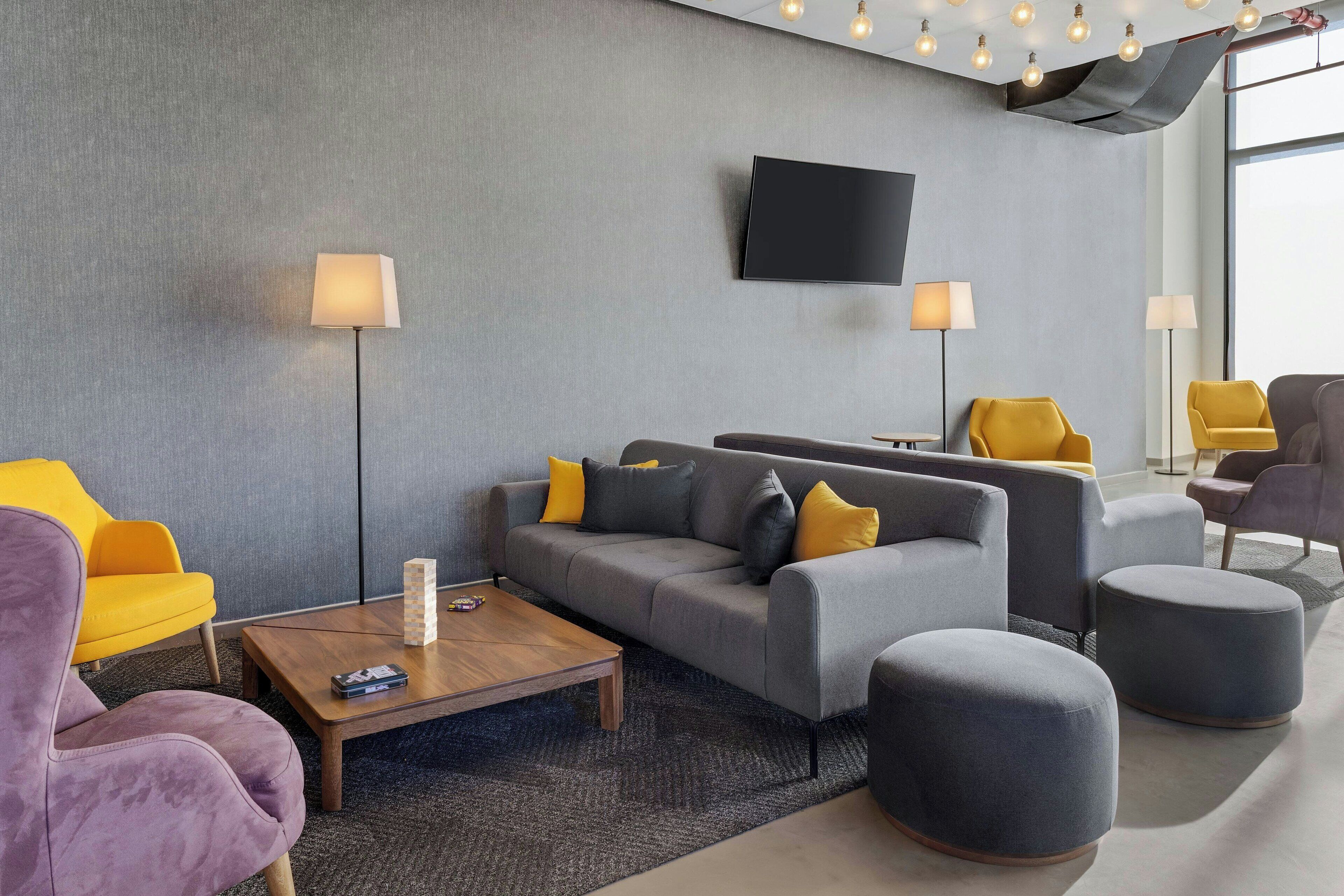A modern living room with a grey sofa, yellow armchairs, a coffee table, and a flat-screen TV mounted on the wall.
