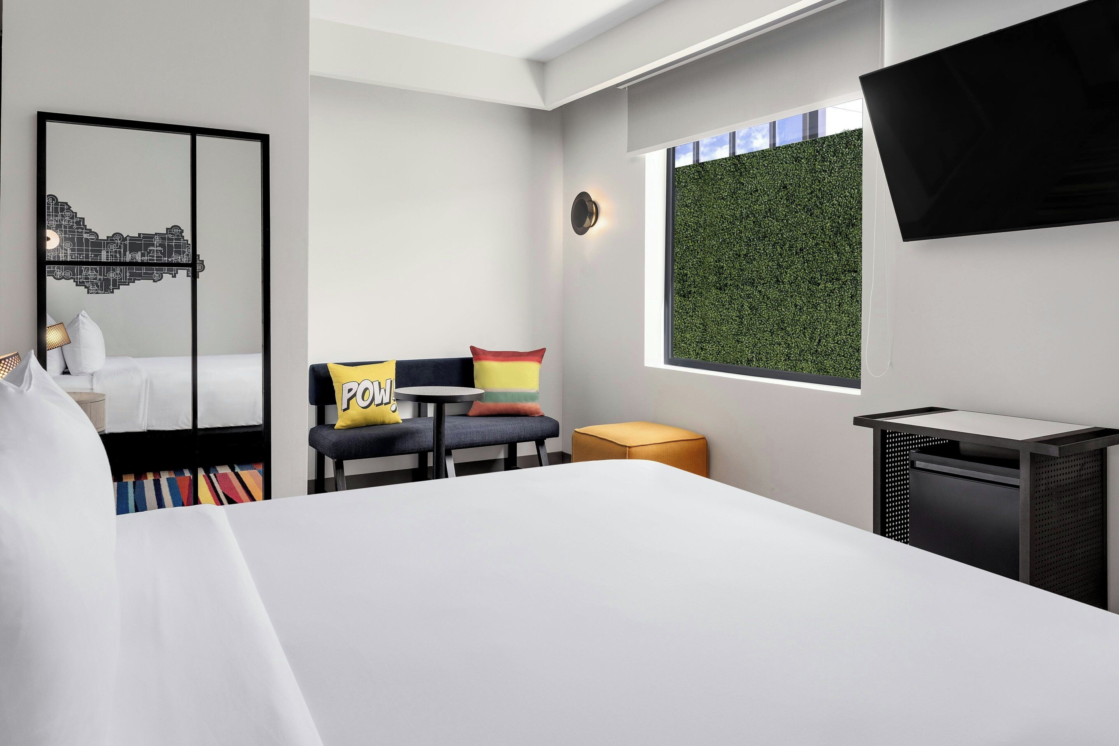 Een moderne hotelkamer met een groot bed, een bureau, een stoel, een klein tafeltje en een aan de muur bevestigde televisie.