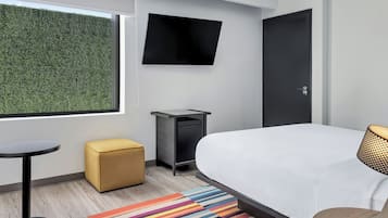 Quarto de hotel moderno com uma cama grande, televisão de tela plana fixada na parede, uma escrivaninha pequena e uma janela com vista para um sebedo verde.