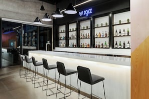 A bar area with a long counter, black bar stools, and shelves of bottles. - Aloft by Marriott Santo Domingo Piantini (Santo Domingo)