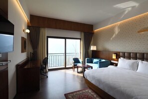 A hotel room with a bed, a desk, a chair, a sofa, and a TV.