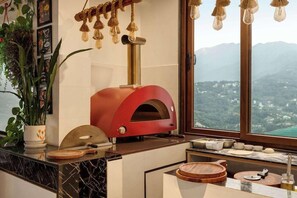 A kitchen with a red wood-fired oven, marble countertops, and a view of mountains through a large window. - Days Inn by Wyndham Gangtok Tadong (GANGTOK)