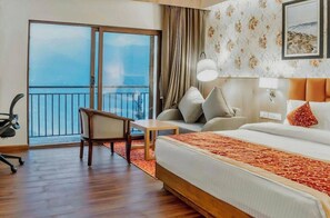 A hotel room with a bed, a desk, a chair, a balcony with a view, and a wall with a floral pattern. - Days Inn by Wyndham Gangtok Tadong (GANGTOK)