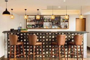 A bar area with a marble countertop, four stools, and a wall of liquor bottles.