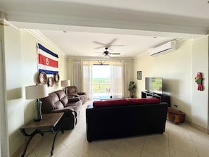 A living room with a sofa, a TV, a ceiling fan, and a flag on the wall.