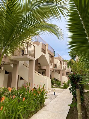 A pathway leading to a building with multiple balconies, surrounded by lush greenery and flowering plants. - High Tide 2 bed/1 bath condo + Terrace (Playas Del Coco)