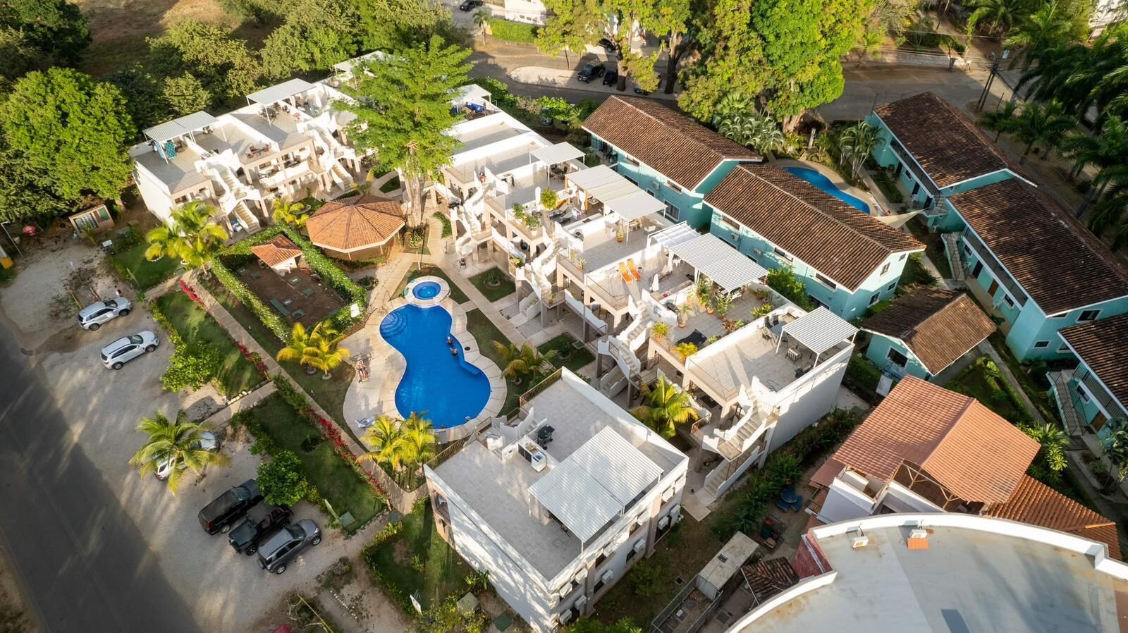 An aerial view of a residential area with multiple buildings, a swimming pool, and parked cars.