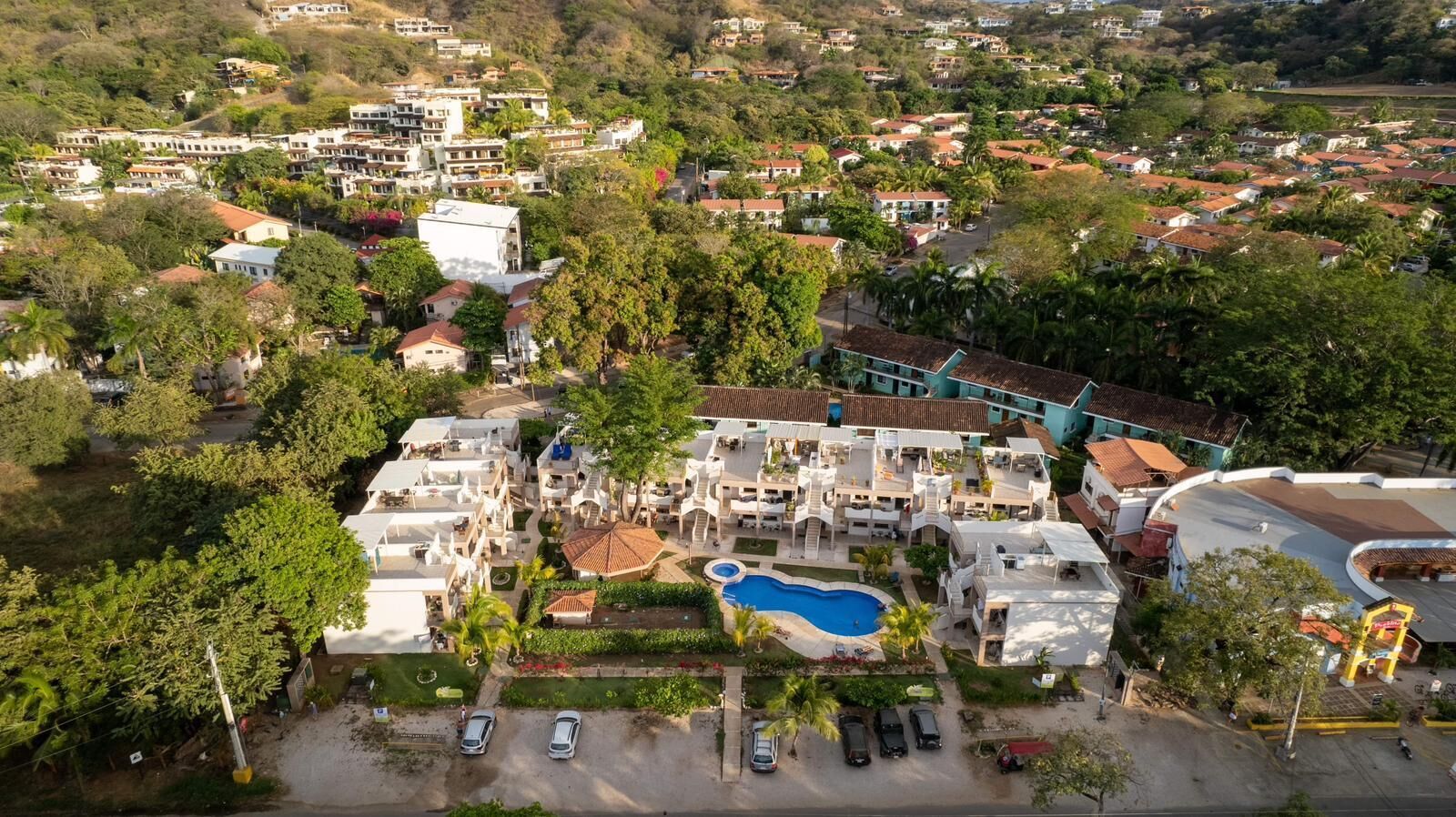 An aerial view of a resort with multiple buildings, a swimming pool, and lush greenery.