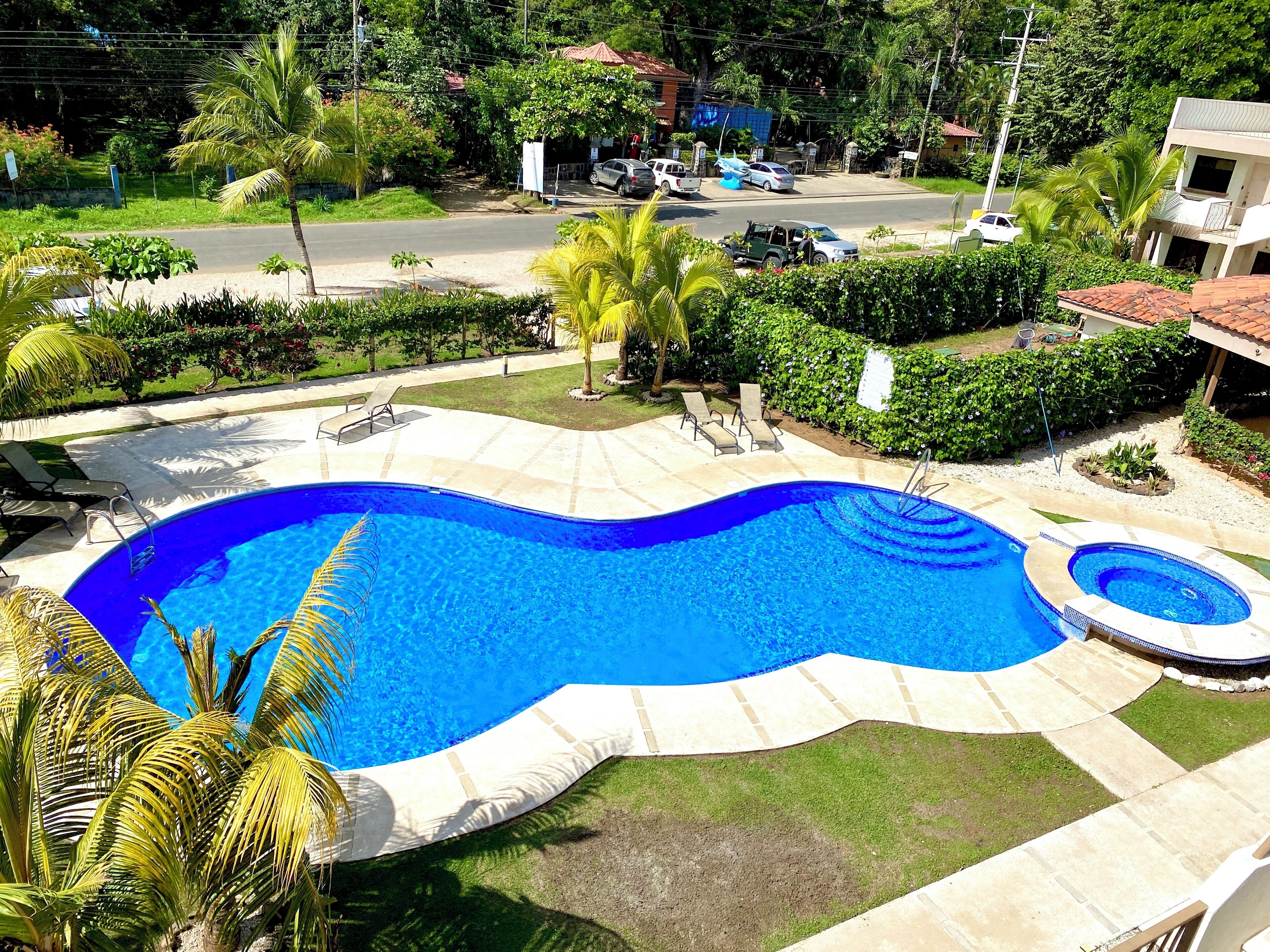 Une piscine à bordures ondulées, entourée d’un patio aménagé avec des chaises longues et un petit jacuzzi circulaire.