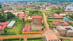 An aerial view of a residential area with a prominent multi-story building with a red roof, surrounded by smaller houses with red roofs, and lush greenery. - The Spot Hotel (Mbale)