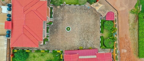 An aerial view of a property with a central open space, surrounded by buildings with red roofs, green landscaping, and a dirt road.
