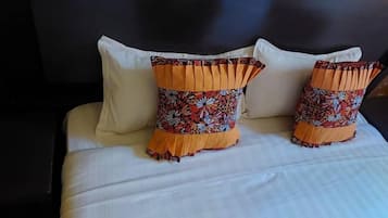 Una cama con sábanas blancas y dos almohadones decorativos con estampado floral y flecos anaranjados.