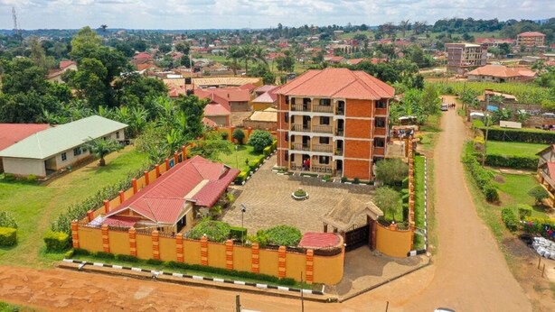 A multi-story building with a red roof, surrounded by greenery and a paved road. - The Spot Hotel (Mbale)