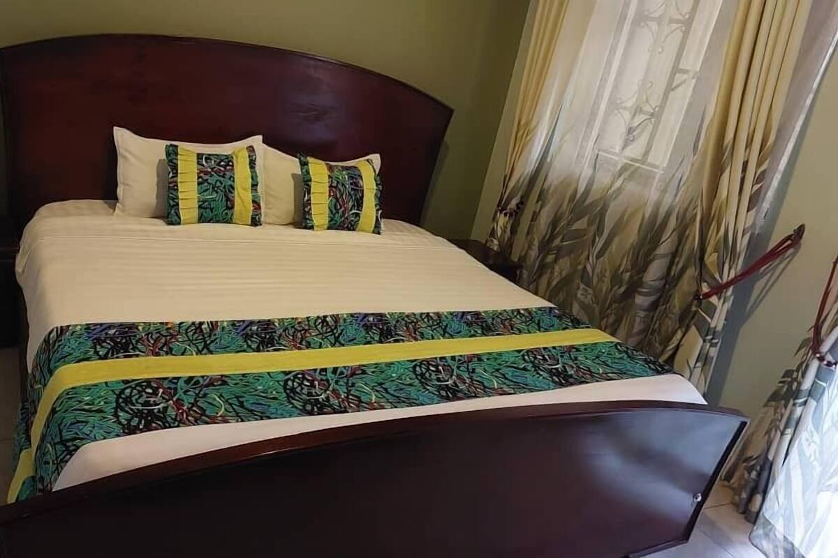 A neatly made bed with a patterned bedspread and pillows, a wooden headboard, and a nightstand with a drawer.