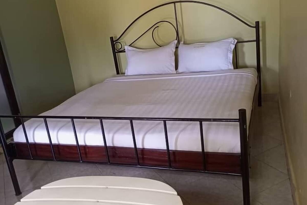 A single bed with a metal frame and white bedding, a small white table, and a chair in a room with green walls.