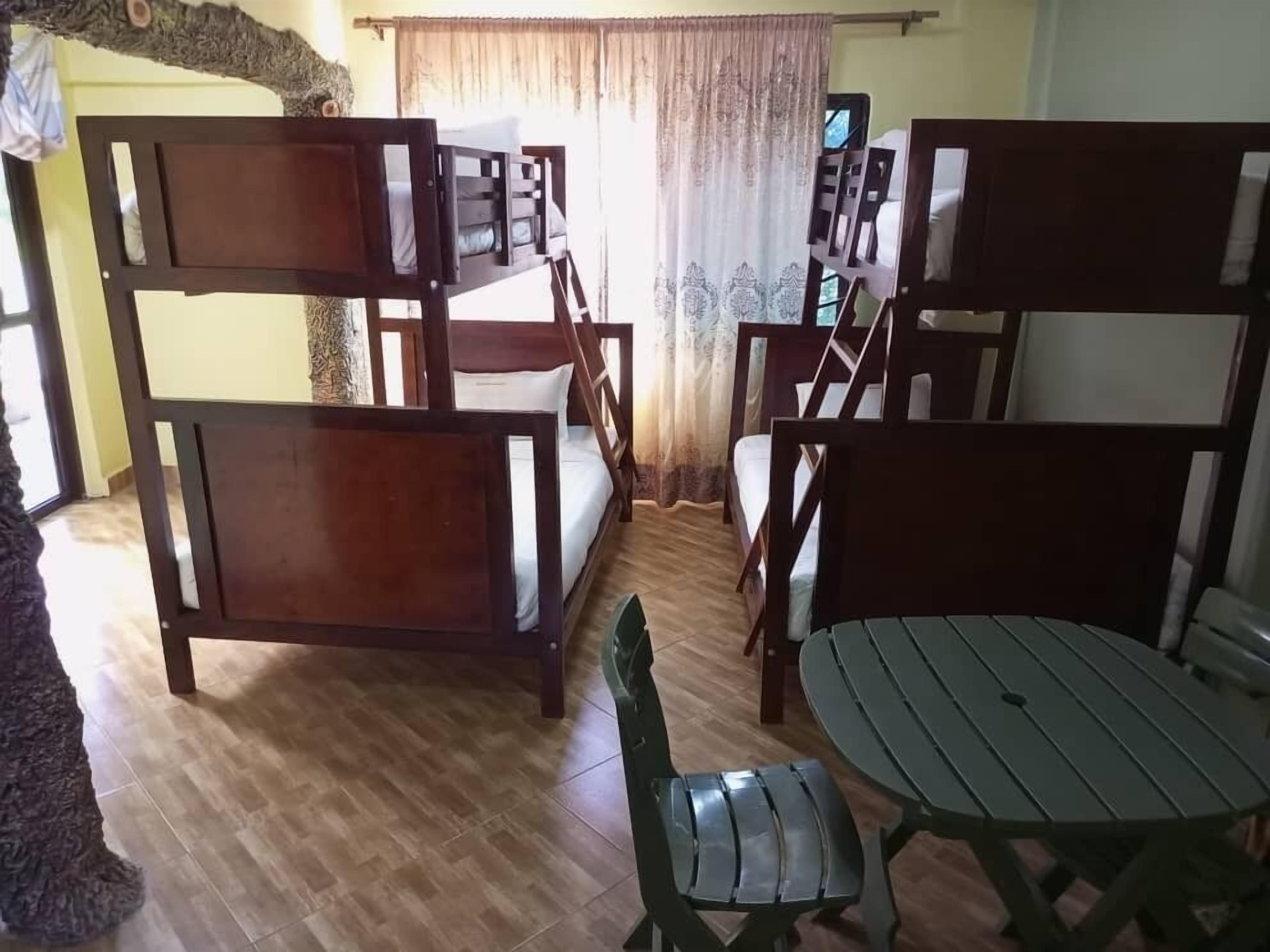 A room with a wooden bunk bed, a green chair, a round table, and a television.