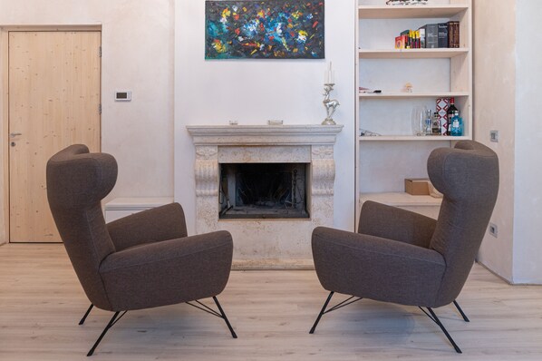 Une pièce comprenant deux fauteuils modernes, une cheminée, une bibliothèque et une porte.
