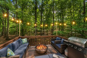 An outdoor deck with a fire pit, grilling station, and seating area surrounded by trees. - 5BR Modern Poconos Game House,  Hot Tub, Fire Pit!
 (East Stroudsburg)