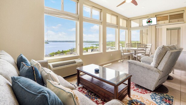 Ein geräumiges Wohnzimmer mit großem Fenster und Blick auf ein Gewässer sowie eine Deckenleuchte und die umliegende Landschaft.