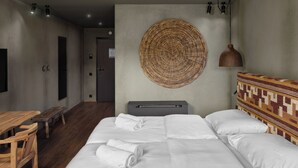 Een hotelkamer met een groot bed, een houten bankje, een tafel en een geweven kunstwerk aan de muur.