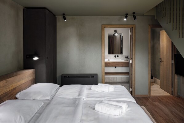 A modern bedroom with a large bed, a wooden headboard, a built-in wardrobe, a vanity with a mirror, and a small desk.